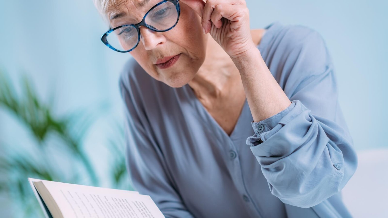 Elderly woman adjusting glasses while reading a book, with text about cataract symptoms, causes, and treatments. Logo for Aarya Eye Care is displayed.