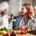 A woman and two children in a kitchen preparing vegetables for a healthy meal aimed at children.