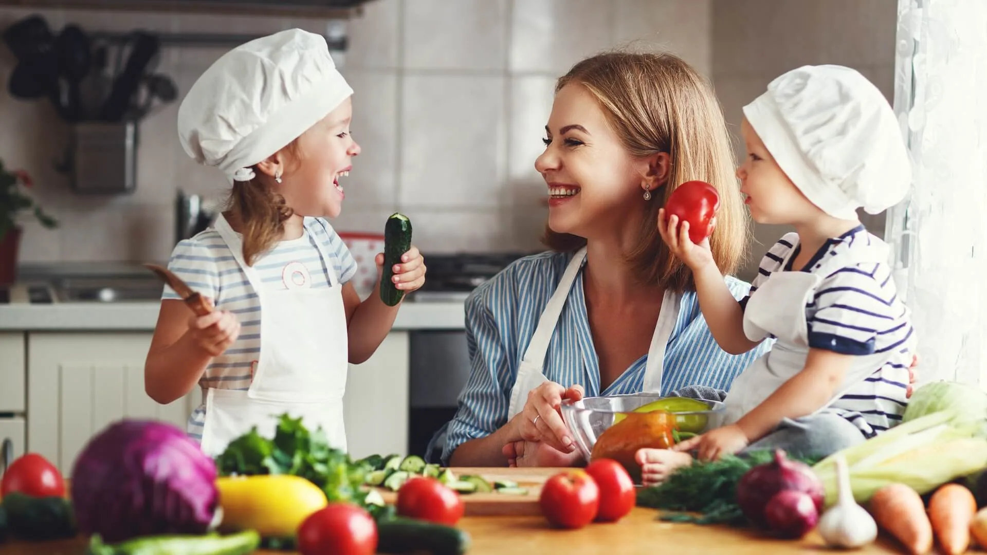 A woman and two children in a kitchen preparing vegetables for a healthy meal aimed at children.