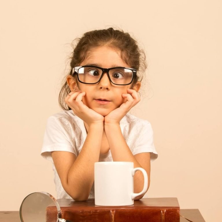 A young girl with oversized glasses rests her chin on her hands, a white mug on the table. Text beside her reads: "Squint: Everything You Should Know About Causes, Symptoms, and Treatment.